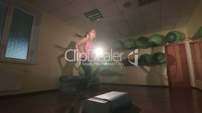 Low-angle shot of young woman training in gym doing step aerobics