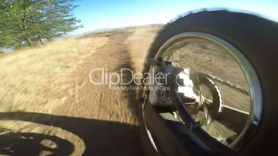 Enduro racer riding bike on dirt track kicking up dust rear wheel point of view