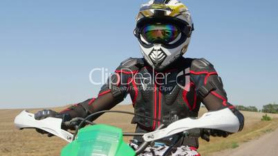 Motocross racer in motorcycle gear riding bike on rural road