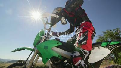 Enduro racer starting engine of his dirt bike riding away against sun