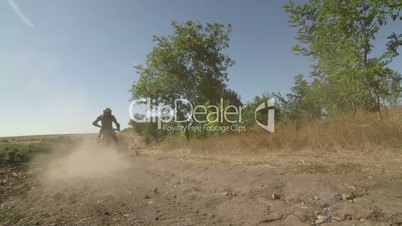 Motocross biker riding enduro motorcycle on dirt track kicking up dust