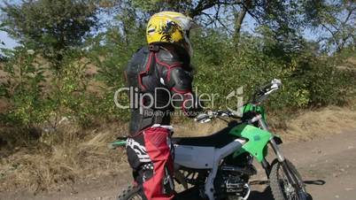Enduro racer starting engine of his motorbike riding away on dirt track
