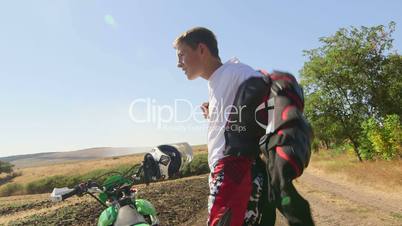 Young enduro racer dressing motorcycle protective gear beside his dirt bike