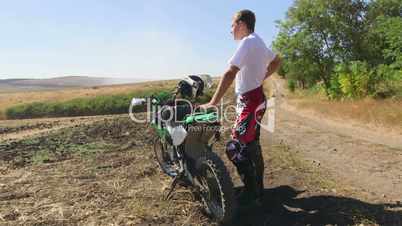 Young enduro racer stands next to his dirt bike looking afar