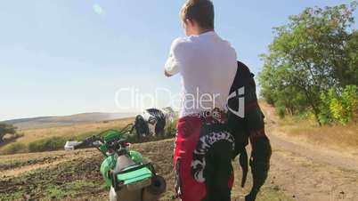 Young enduro racer puts on chest protector beside his dirt bike