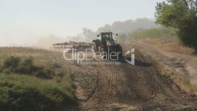 Farmer using modern farm tractor with disk harrows for harrowing field