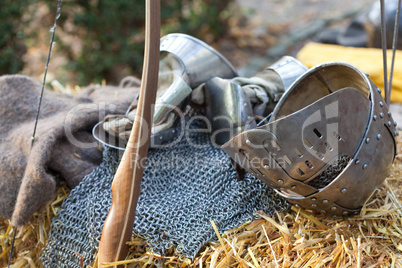 A silver metal helmet, gloves, mesh vest and bow lying in straw