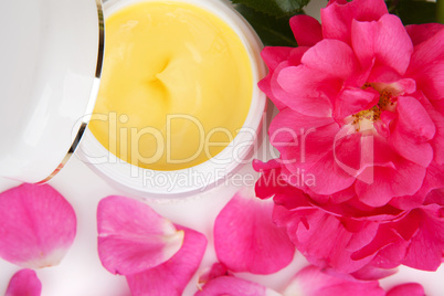 Open jar with the cosmetic cream and rose petals isolated on whi