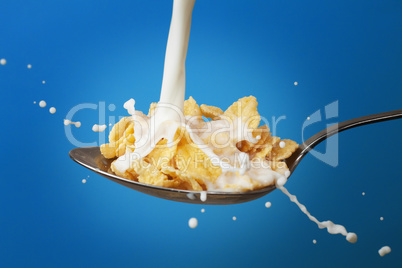 milk splashing into spoon full of cornflakes