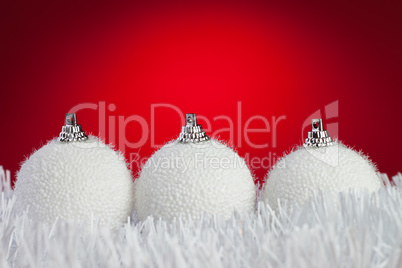three white christmas balls on tinsel over bright red background