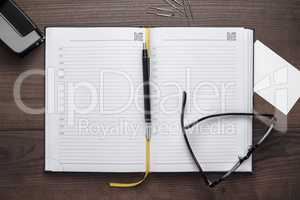 personal organizer and pen with glasses on the table