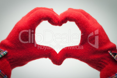 hands in red gloves show heart shaped sign over grey