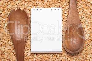 notebook for recipes and wooden spoons over peas background