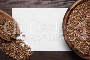 buckwheat over brown wooden background and blank sheet of paper