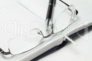 opened business diary with pen and glasses over white background