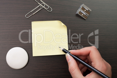 woman writing with pencil on yellow sticker