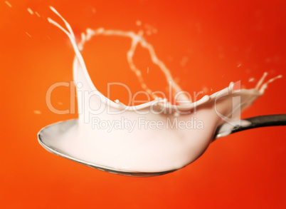 yoghurt splash in the spoon over orange background