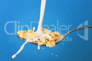 milk splashing into spoon with cornflakes over blue