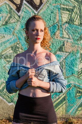 Schutzbedürftige junge Frau, steht vor einer Graffitti Mauer