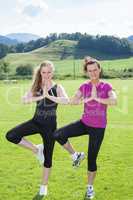 Zwei Frauen stehen in der Yoga-Baum-Haltung in einem  Feld