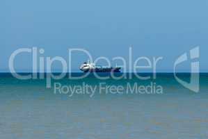 Cargo ship in distance on water fading into brown shallows