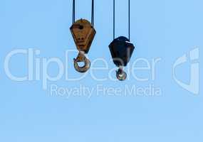 Pair of hanging industrial crane hoists on pale blue sky