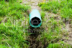 Plastic green drain pipe emerging from grassy ground
