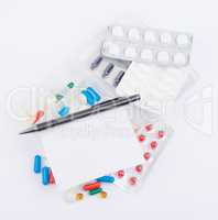 Tablets, capsules in blister packs and ballpoint pen with blank sheet of paper