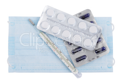 Tablets and capsules in blister packs with a thermometer lying on the face mask