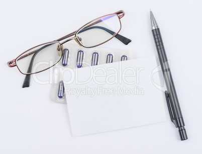Glasses and tablets. White sheet with a ballpoint pen