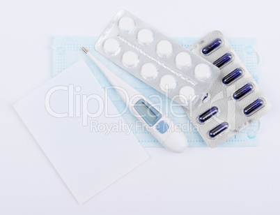 Tablets, capsules in blister packs with thermometer and white sheet of notebook