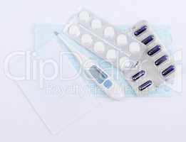 Tablets, capsules in blister packs with thermometer and white sheet of notebook