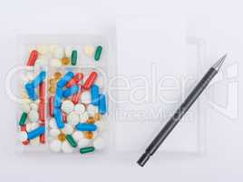 Pills, capsules in glass box with white paper sheet and ballpoint pen
