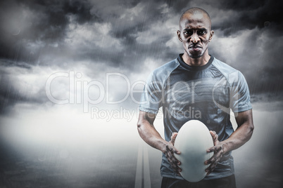 Composite image of portrait of serious athlete holding rugby bal