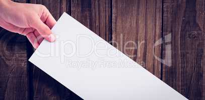 Hand holding white paper against wooden wall