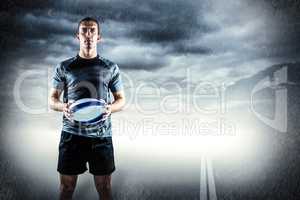 Composite image of serious rugby player in black jersey holding