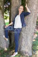 Junge Frau in einer blauen Jacke lehnend gegen Bäume