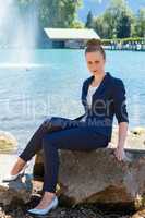 Junge Geschäftsfrau sitzt auf einen großen Felsen am See