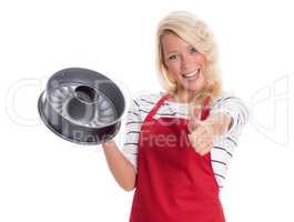 Hausfrau in Schürze hält eine Kuchenform und zeigt Daumen hoch