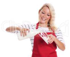Hausfrau in Schürze gießt Frischmilch in ein Glas