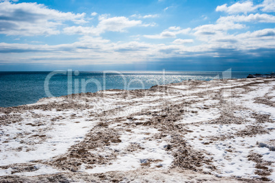 Dirty ice field near water under partly cloudy blue sky