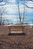 Empty wood bench at lake and bare trees in winter