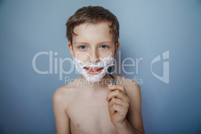 Boy  teenager European appearance   shaves face on a gray