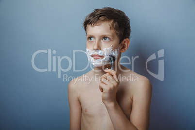 Boy  teenager European appearance shaves face on a gray