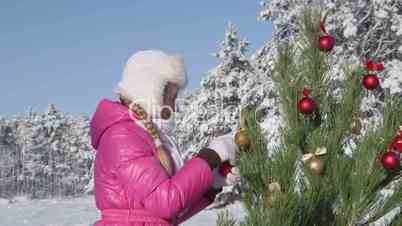 Child decorating Christmas tree in snow covered winter forest