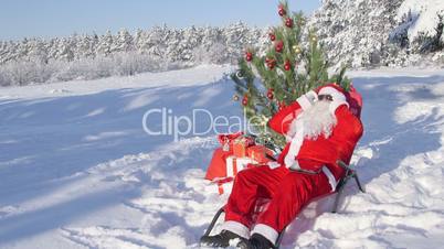 Santa Claus near Christmas tree enjoying frosty sunny day in snow