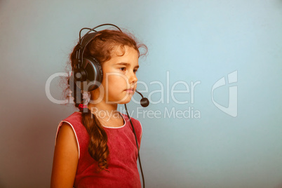 Teen girl child in headphones with a microphone on a blue backgr