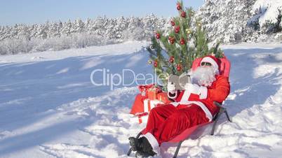 Santa Claus with gift bag using tablet computer in snow covered winter forest