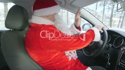 Man in Santa Claus costume driving car in snow through winter forest