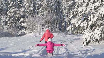 Mother pulling child on sled through snow in winter forest